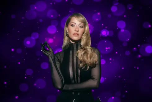 Kaya Hotels artist photo: Derya Uluğ with long blonde hair in black against a purple bokeh background