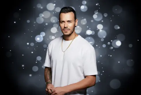 Kaya Hotels artist photo: Deha Bilimlier in a white T-shirt against a silver bokeh background