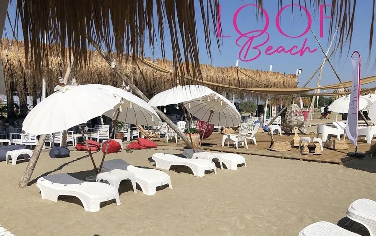 تخت‌های آفتاب و چترهای سفید روی شن جلوی بار LOOF Beach