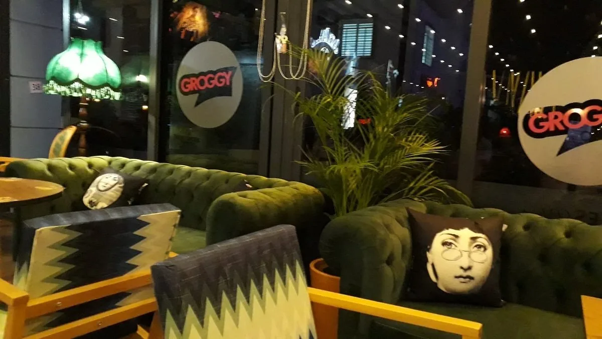 Green velvet sofas by the windows of Groggy Lounge in Girne, with Groggy signs on the glass