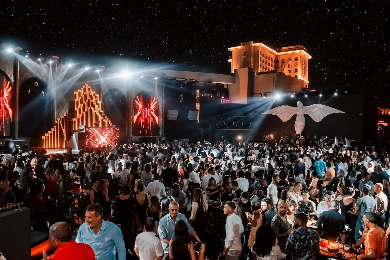 Packed open-air dance floor at Odyssey Club with the winged angel statue and Lord's Palace Hotel lit up behind