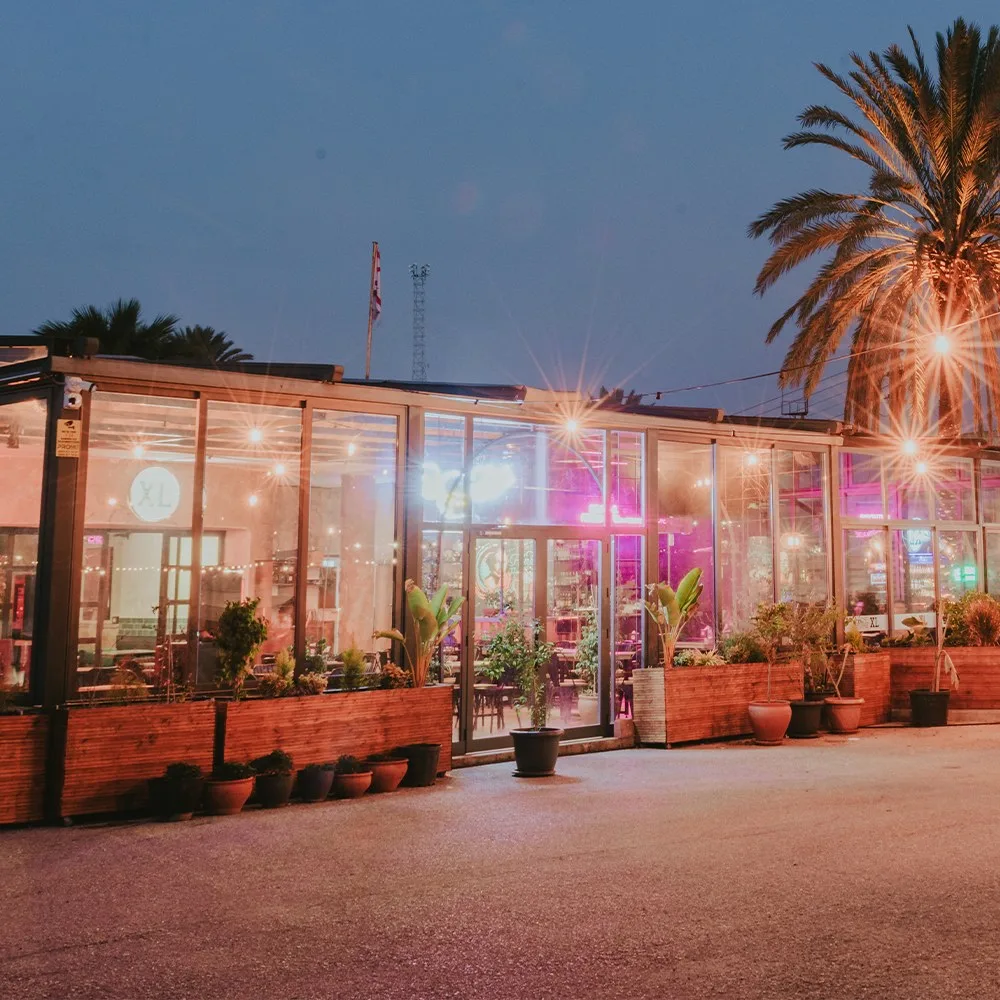 Glass-fronted Hamburg XL restaurant on Zahra Street, Lefkoşa, lit up at dusk with palm trees