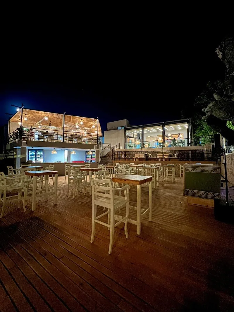 Chill Beach's wooden deck with high tables at night and its two-level bar building lit up behind