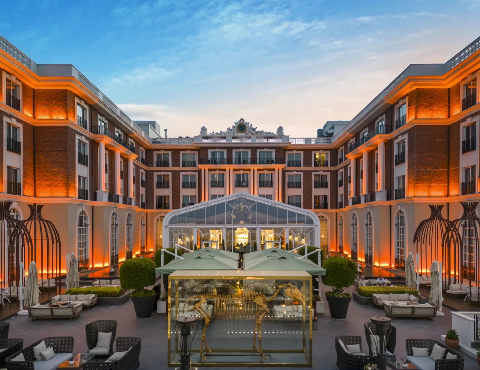 Kaya Palazzo Girne's palace-style courtyard at dusk, lit in orange, with a glass pavilion and lounge seating
