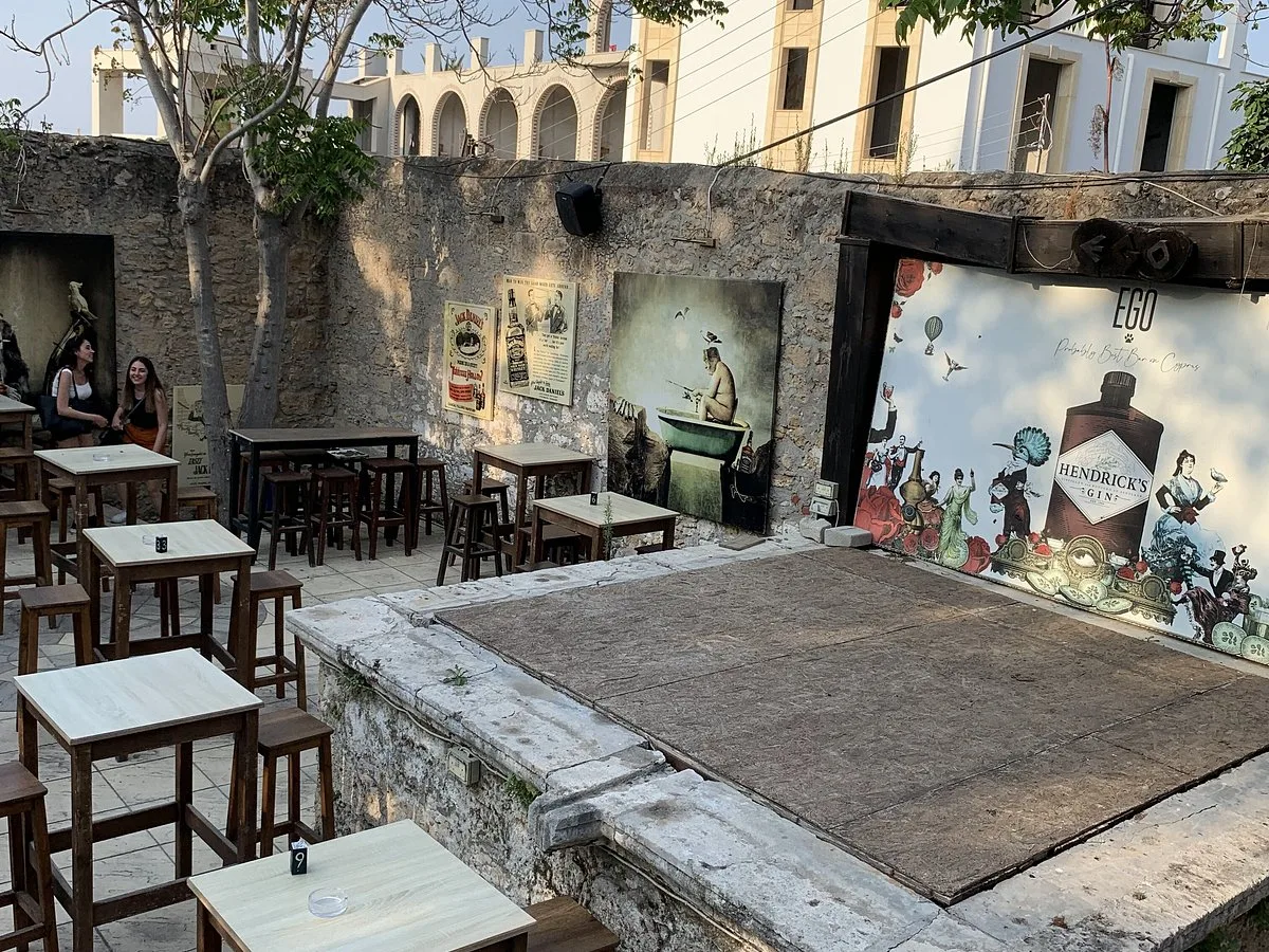 Ego Bar courtyard in Girne: stone walls, wooden high tables and stools, and an outdoor stage with an EGO backdrop