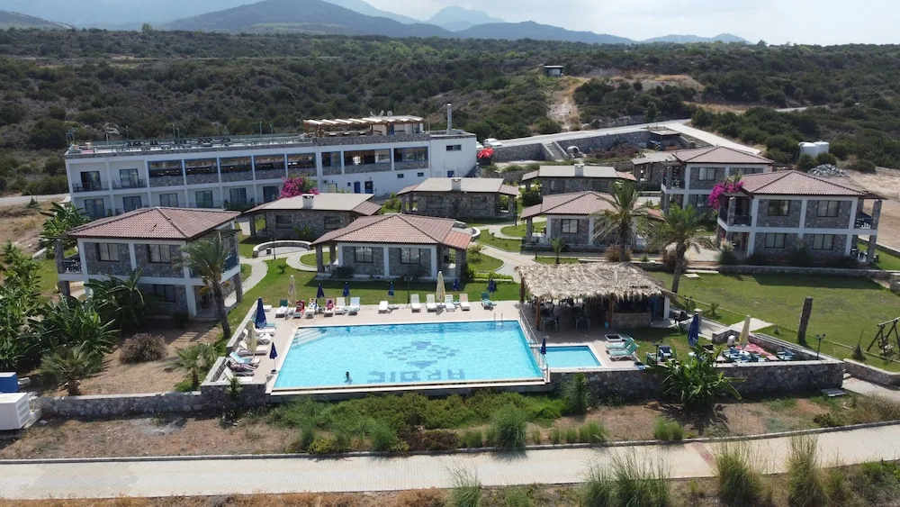 Tatlısu'daki Ardıç Ağacı Tatil Köyü'nün havadan görünümü: ARDIC mozaikli havuzun çevresinde taş evler ve otel binası, arkada dağlar