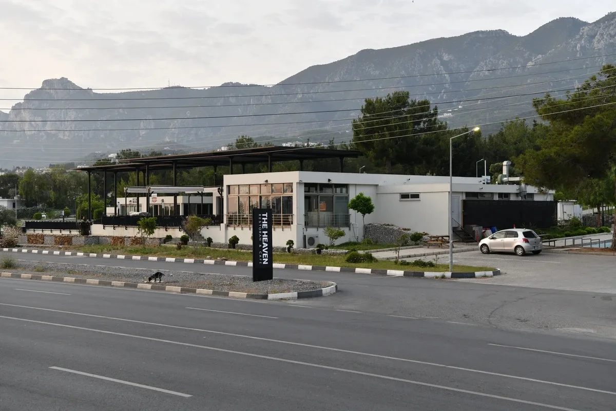 Alsancak'taki The Heaven Restaurant & Cafe: pergolalı terası olan beyaz tek katlı bina, yol kenarında 'THE HEAVEN' tabelası ve arkada Beşparmak Dağları