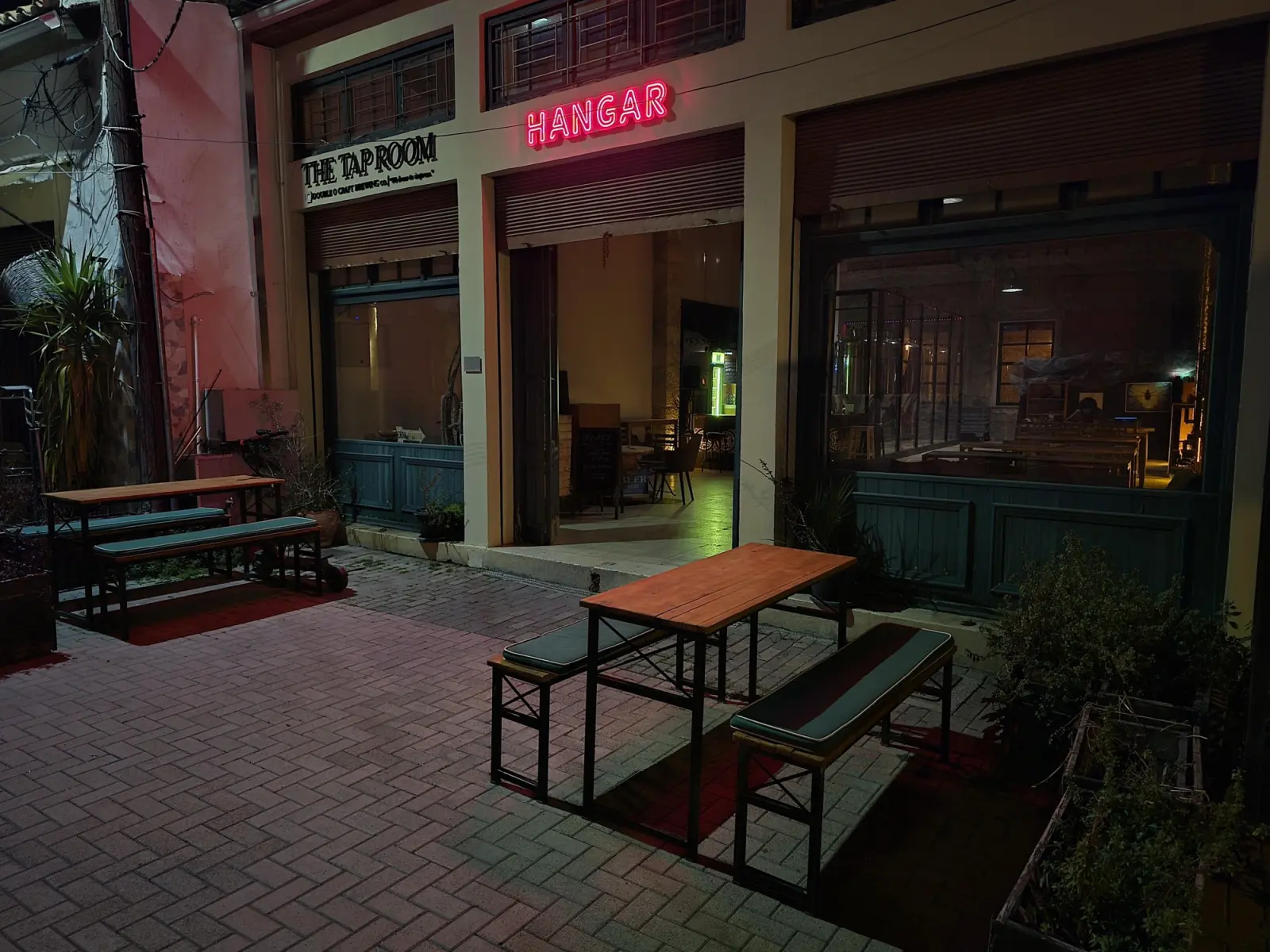 Hangar Culture Space at night: neon HANGAR sign and The Tap Room front with wooden benches on the pavement, Yeşil Gazino Sokak, walled city of Nicosia