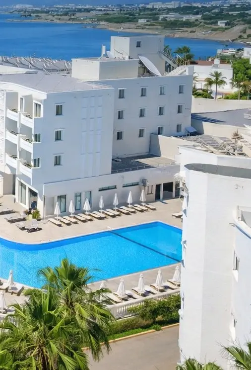 Vuni Palace Hotel in Kyrenia: white hotel building above the pool with sun loungers and the sea behind