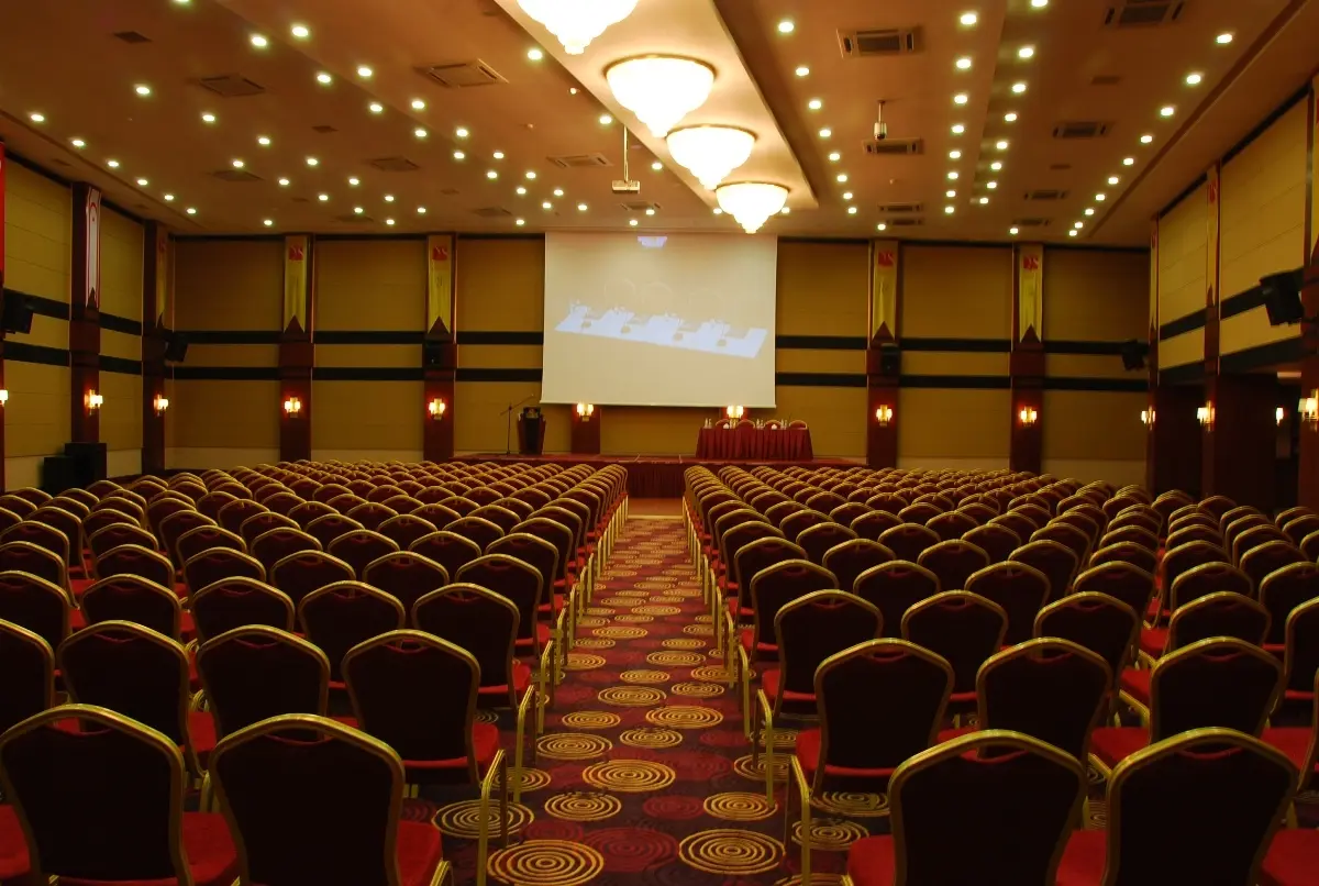Vuni Hall at Vuni Palace Hotel, Kyrenia: auditorium with rows of red-and-gold chairs facing a stage and projection screen
