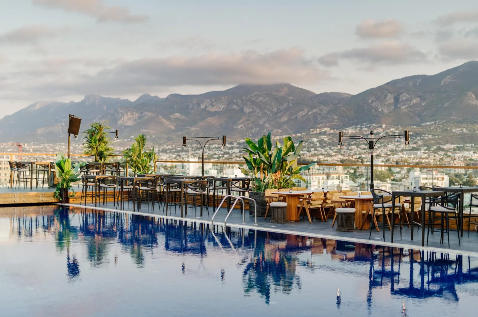 Sky Lounge & Bar rooftop terrace at Lord's Palace Hotel, Kyrenia: pool reflecting palms, lounge tables and the Kyrenia mountains at dusk
